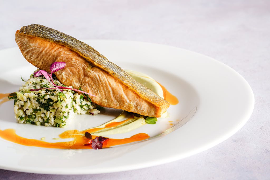 A beautifully plated salmon dish with quinoa, herbs, and a vibrant sauce, perfect for gourmet food lovers.