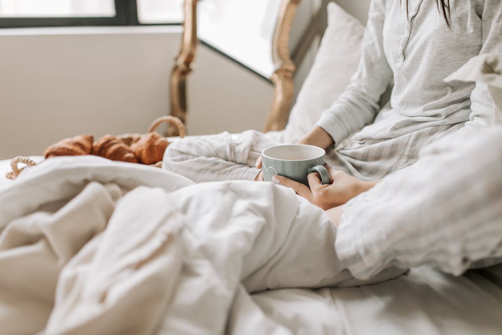 A relaxing morning scene with a woman enjoying coffee in bed with warm blankets and croissants.