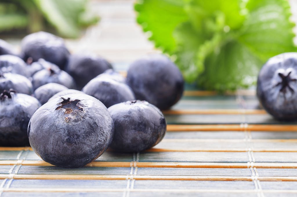 Close-up of fresh blueberries on a bamboo surface with green leaves.