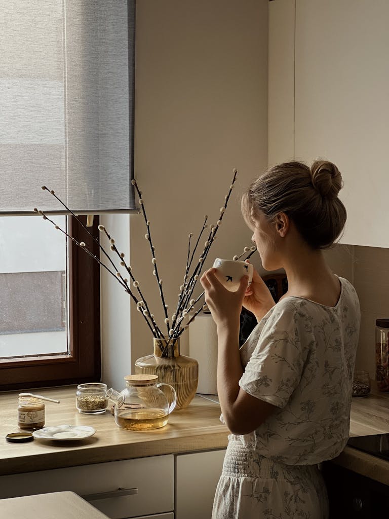 Woman savoring tea in a cozy kitchen with soft natural light.
