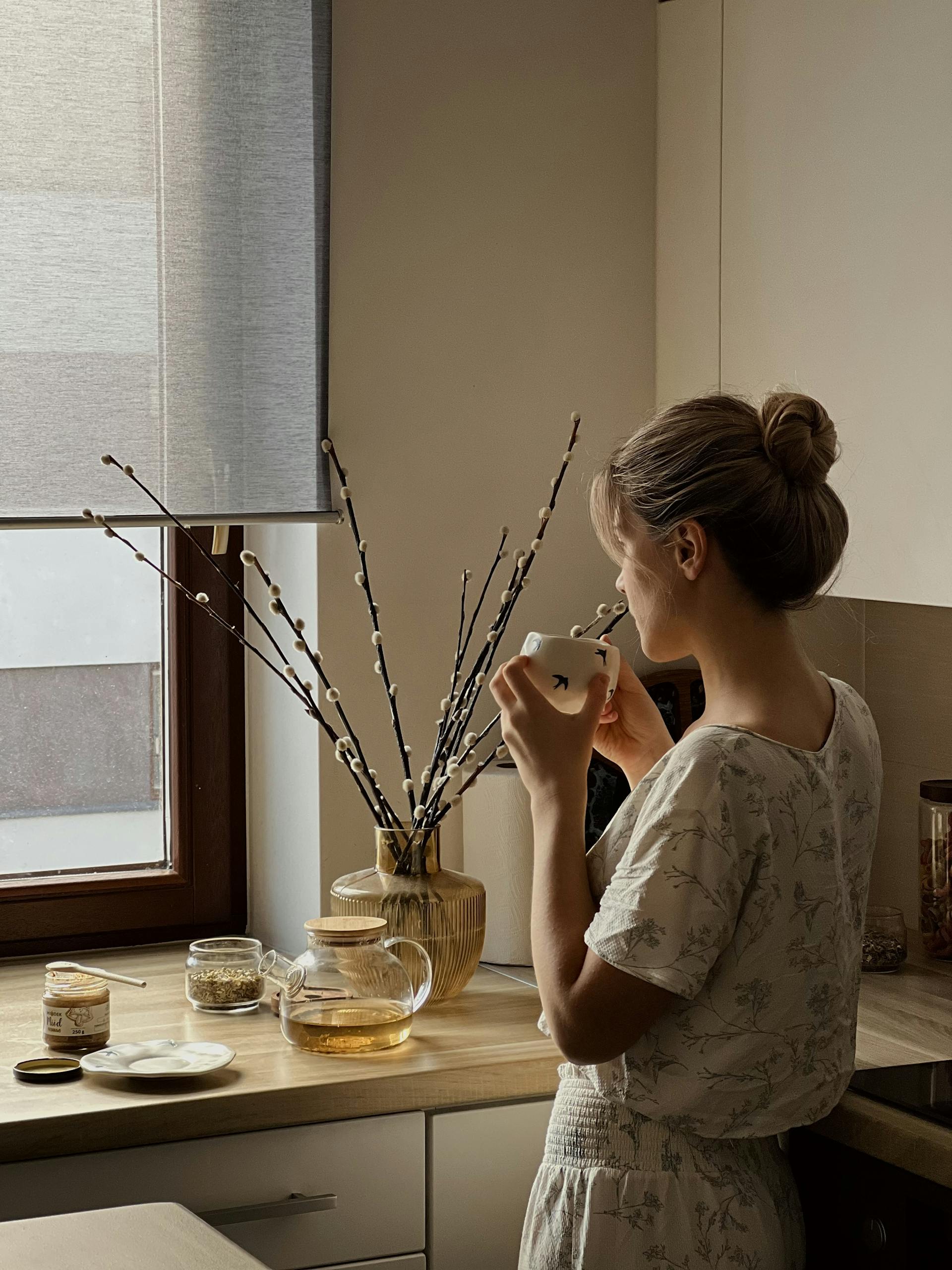Woman savoring tea in a cozy kitchen with soft natural light.
